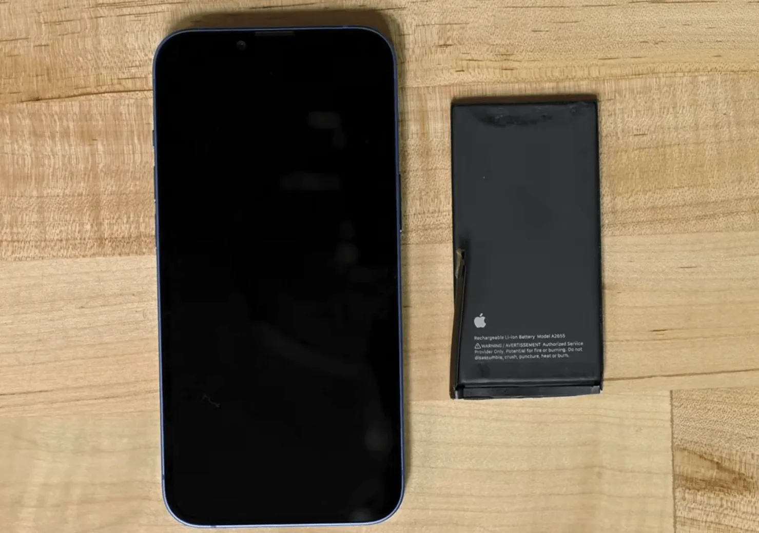 iPhone 13 next to its removed original Apple battery on a workbench
