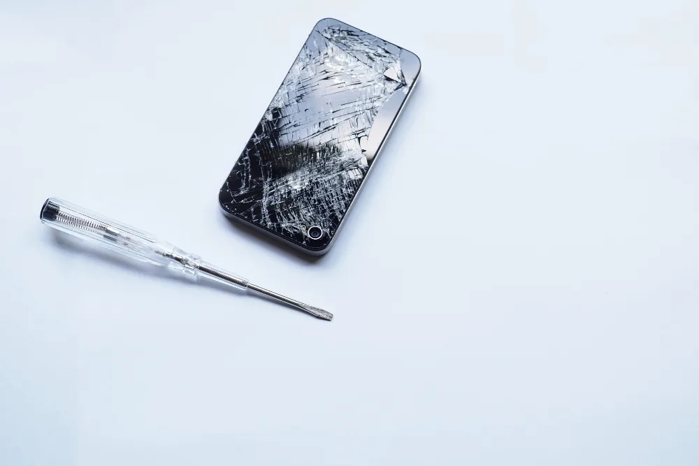 Cracked iPhone next to a repair screwdriver