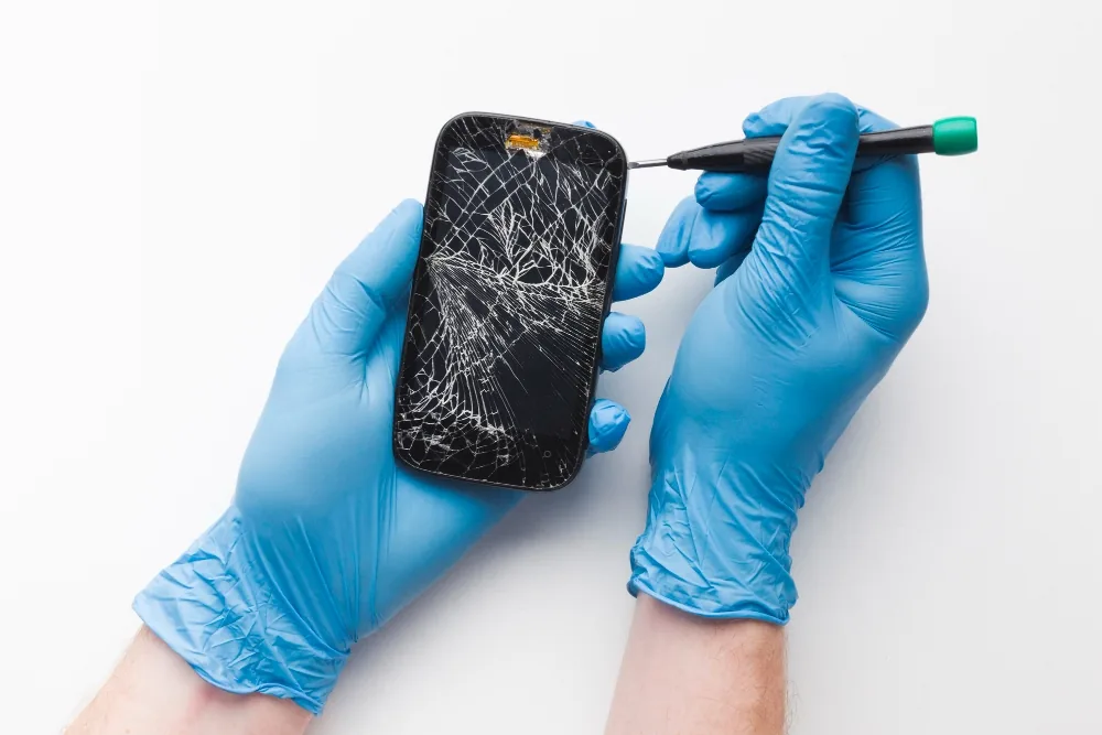 Technician in gloves inspecting a shattered phone screen